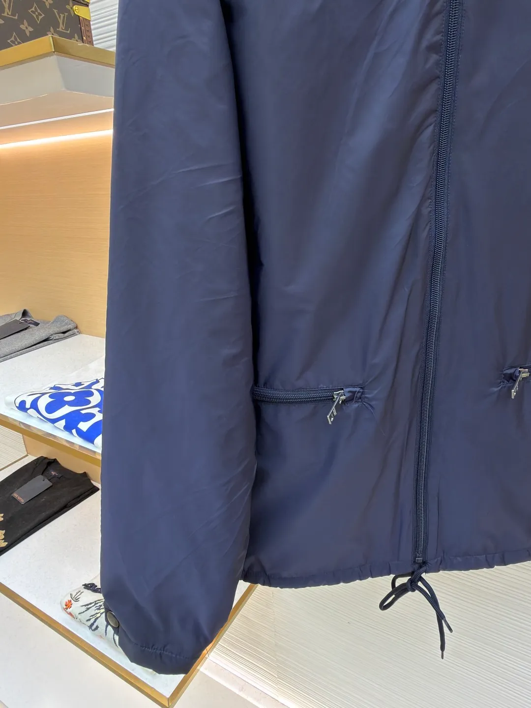 Prada Regenerated Nylon Fleece Jacket ●Original version: Purchased and developed by 12048 ●Item number: 1682331-B70 ●Fabric: Regenerated nylon fabric ●Technology: Made on positioning cutting machine ●Color: Navy blue ●Version: Fitted version ●Weight: about 585 grams ●Size: S-M-L-XL ●Description: High-density yarn is made by melt spinning through a special process. The yarn has been stretched and twisted through multiple processes to give the fabric the stiffness and wrinkle resistance that are comparable to those of native materials, while retaining a light and drapey wearing experience. The surface of the fabric is treated with an environmentally friendly coating process to form a micro-waterproof film layer, which is both windproof and breathable. The main raw material is polyester fiber blended wool raw material which is cleaned and pre-treated to remove impurities. After the yarn is woven into fabric through a loom, it is brushed, that is, the surface of the fiber is fluffed through mechanical brushing to form fluff. Then the shaking process is carried out, and the fabric is shaken under high temperature and humid conditions, so that the fibers form small spherical particles to increase the thermal insulation performance. The shoulder splicing uses twill sewing technology, the raglan sleeve design releases shoulder movement space, and the regular shoulder line ensures the stiffness of the overall silhouette, maintaining an elegant silhouette for both sports and static wear. The three-dimensional pleat design is incorporated into both sides of the body and sleeve elbows, and a long-lasting pleat texture is formed through high-temperature setting technology. This not only enhances the aerodynamic performance of the fabric, but also enriches the visual hierarchy with light and shadow changes, breaking the dull feeling of solid color fabrics. The cuffs are equipped with a hidden snap-button adjustment system, which can be freely tightened according to the circumference of the wrist to prevent cold wind from entering; the straight bottom edge is matched with a drawstring at the hem, and the inner rope buckle design can be used to adjust the tightness, taking into account warmth preservation and waistline shaping. The overall wiring is straight and delicate, the fabric is comfortable and soft, and the color is consistent without color difference. It can be matched with the same style to create a fashionable look and control various occasions. Customized accessories, complete with three standards, same style for men and women!