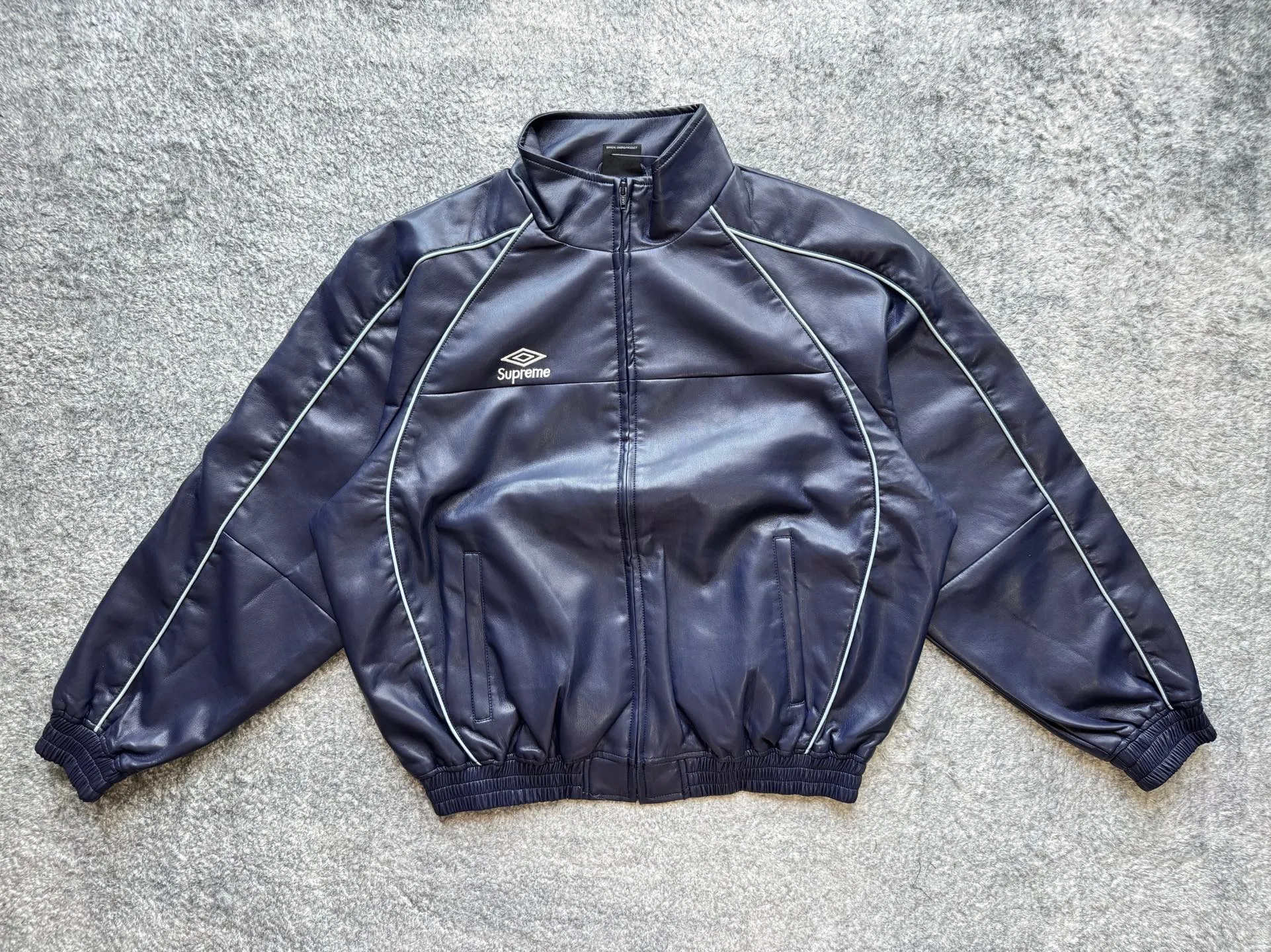 P590 Supreme Umbro joint model FW25 WEEK4 Leather Track Jacket embroidered logo zipper closure leather jacket, same style for men and women, made of lambskin material, mesh lining. Welted zippered hand pockets at lower front and internal chest pocket. Elasticized cuffs and hem in leather. Embroidered logo at chest and back neck. Color: Black, Navy, Pink Size: S M L